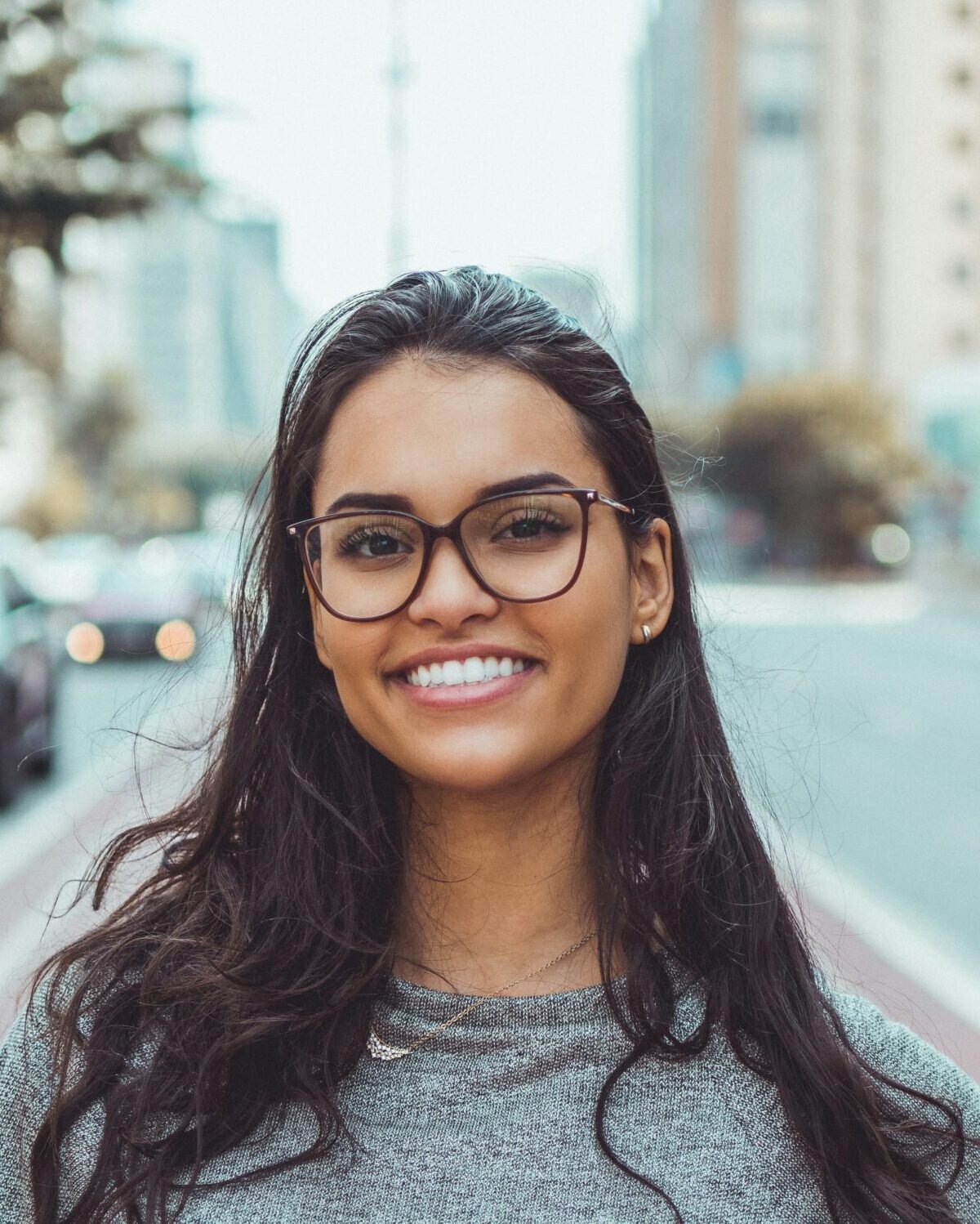 A young woman with glasses smiling on a city street, embracing urban lifestyle.