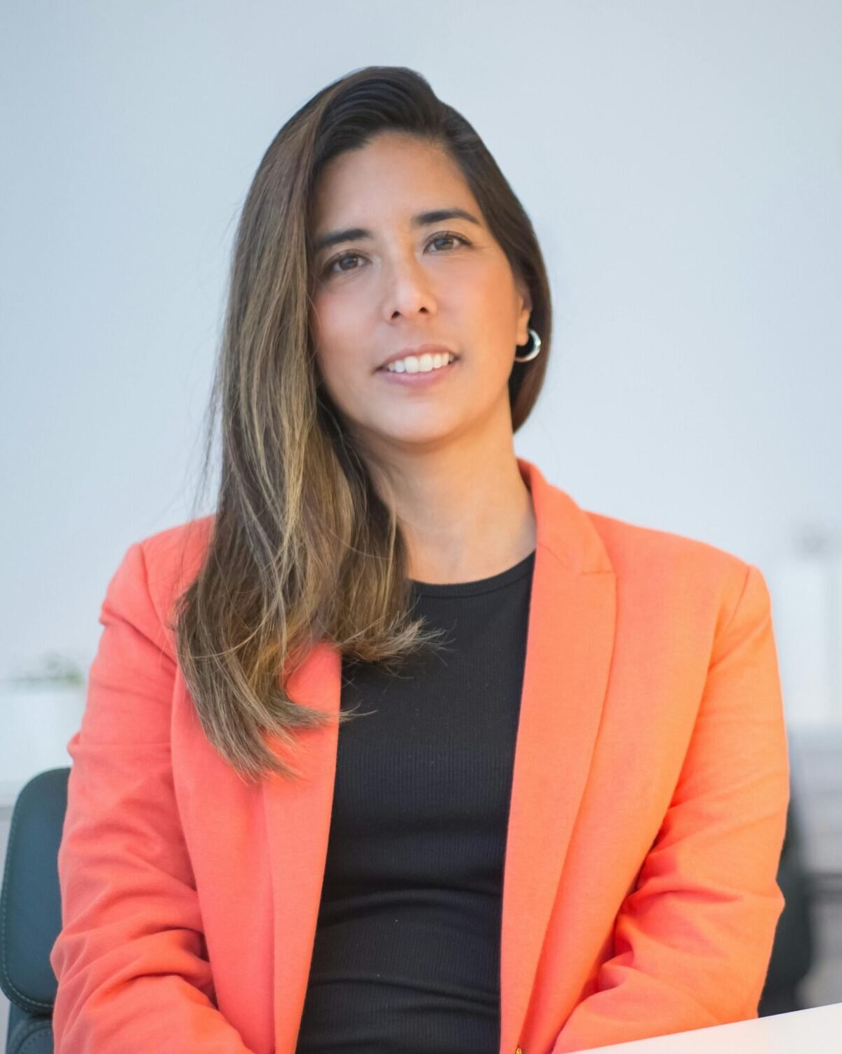 Confident businesswoman wearing a blazer, sitting at a desk in an office environment.